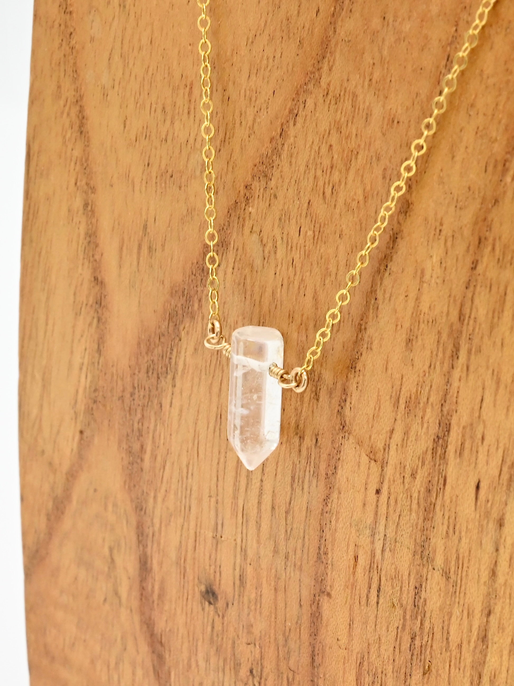 Gold necklace with a clear crystal pendant on a wooden surface