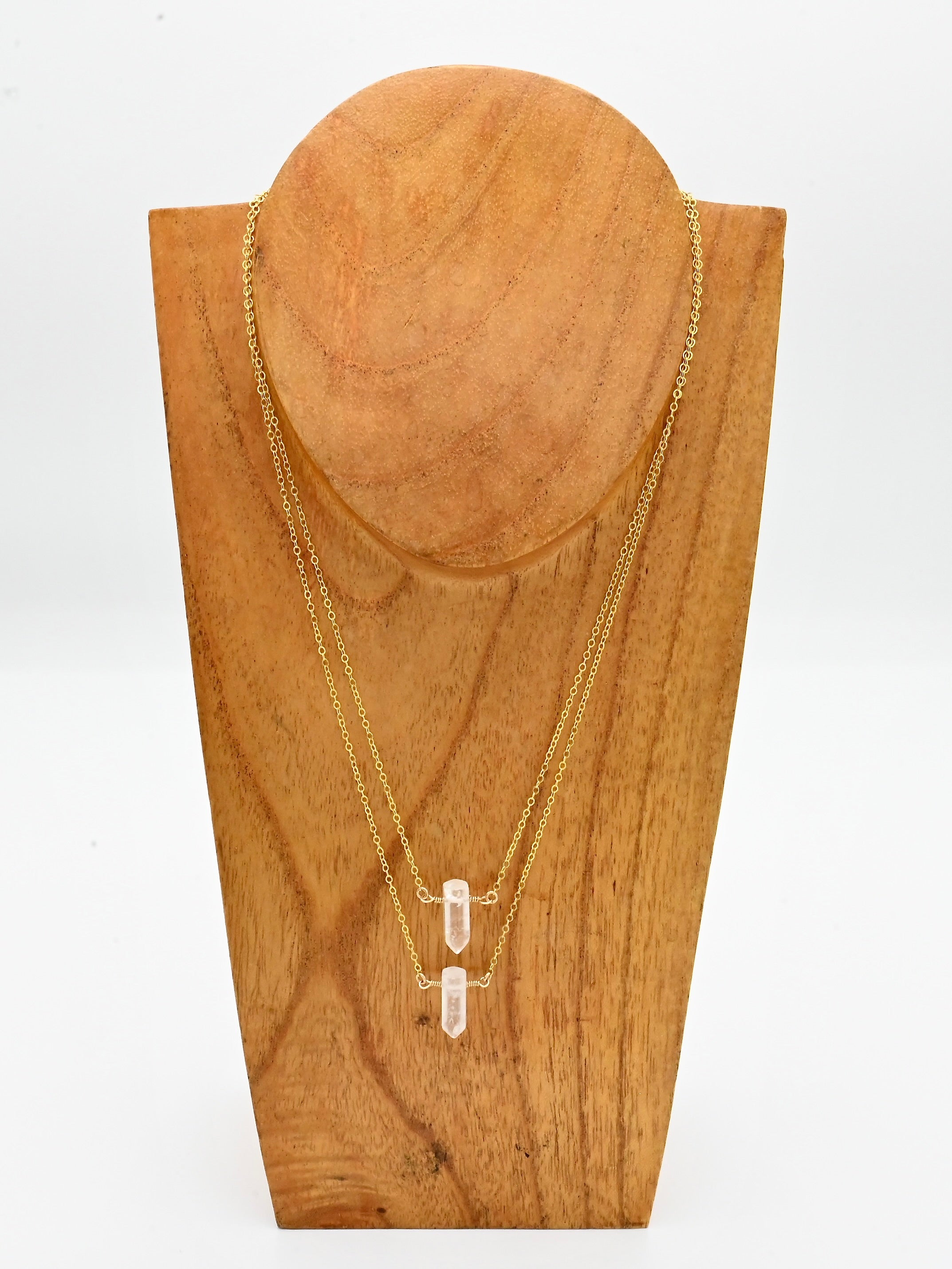 Gold necklace with pendant on a wooden stand against a white background