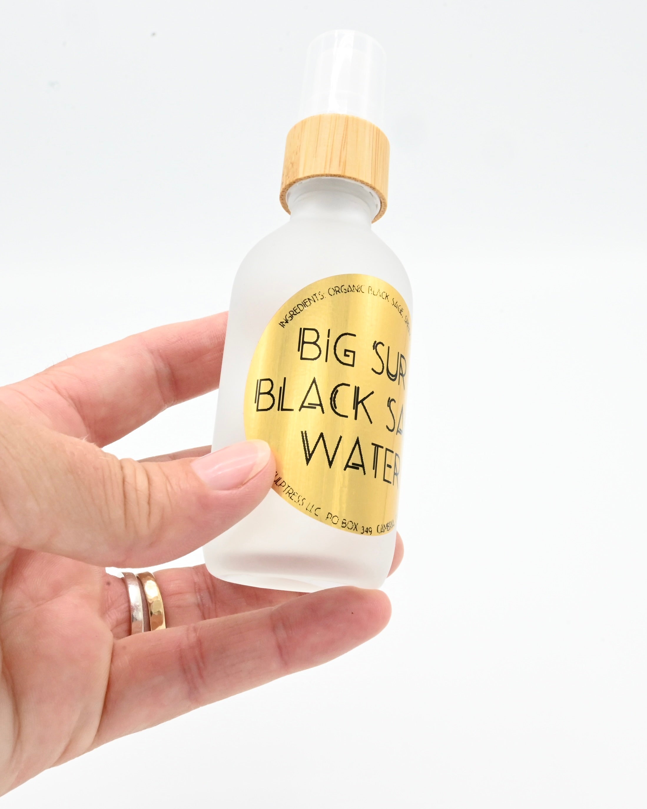 Hand holding a bottle of 'Big Sur Black Salt Water' with a white background