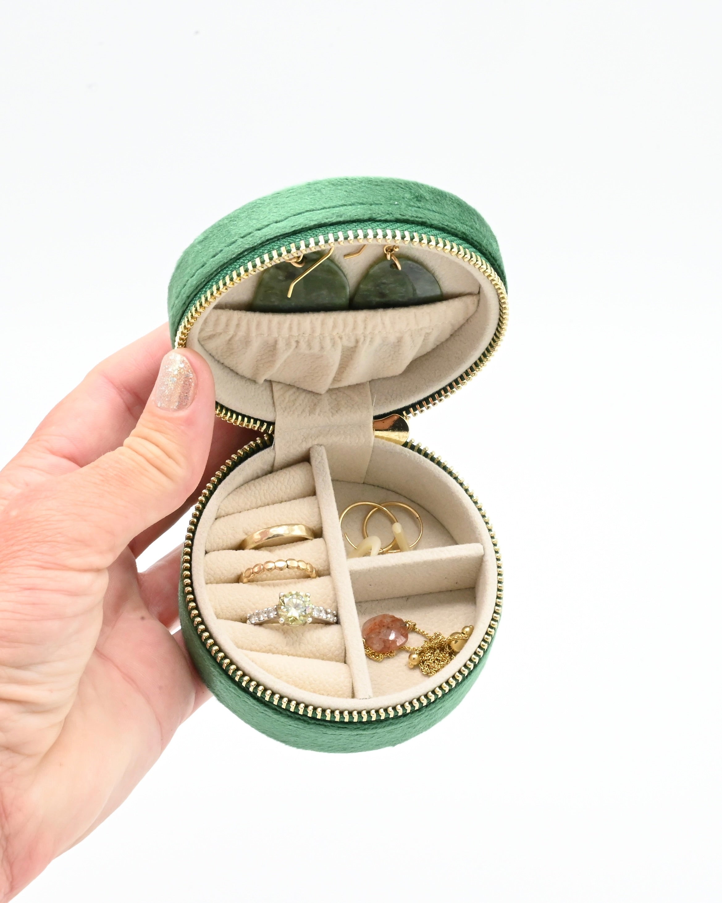 Round green jewelry case with rings and necklaces on a white background