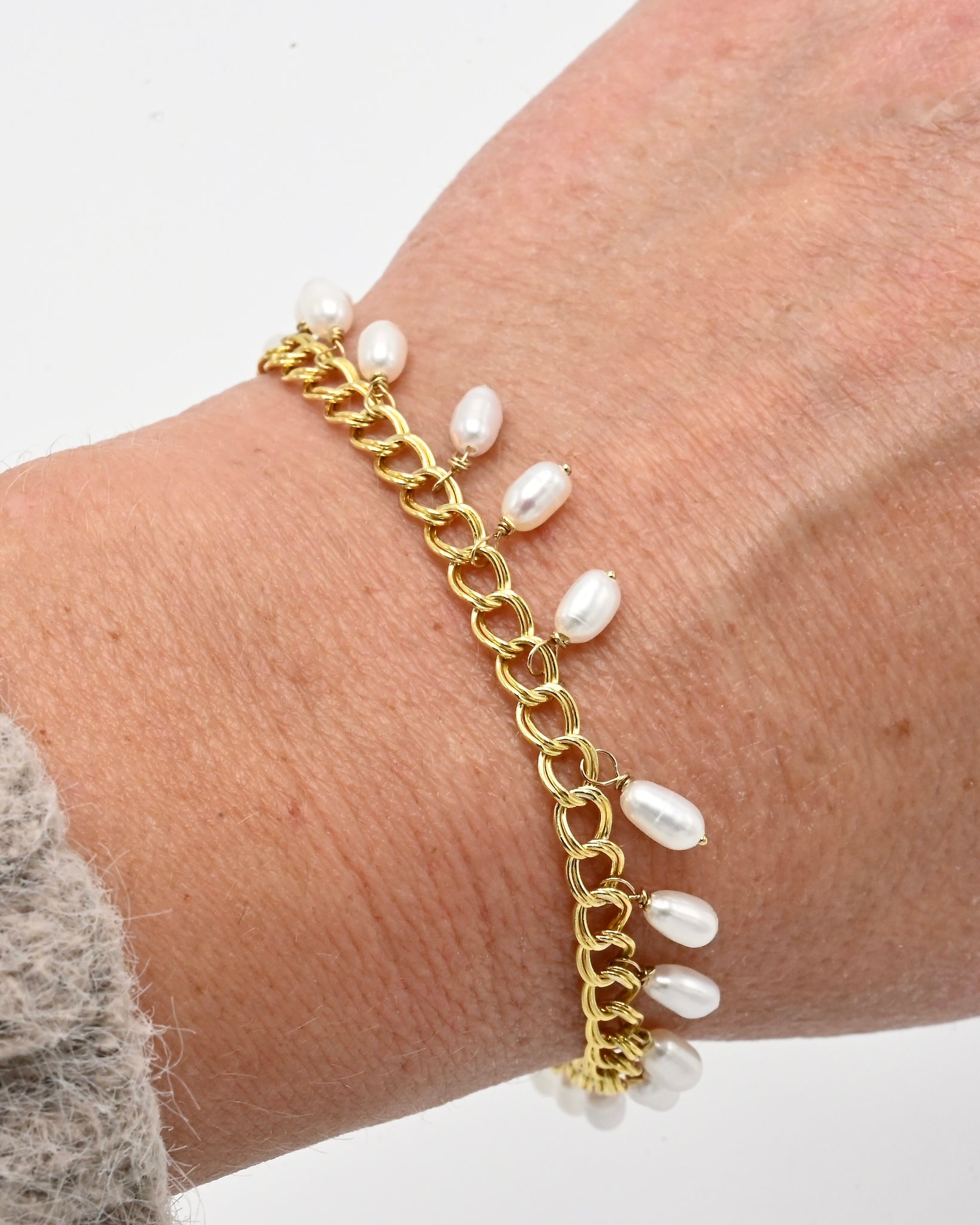 Gold chain bracelet with pearl-like beads on a wrist against a white background
