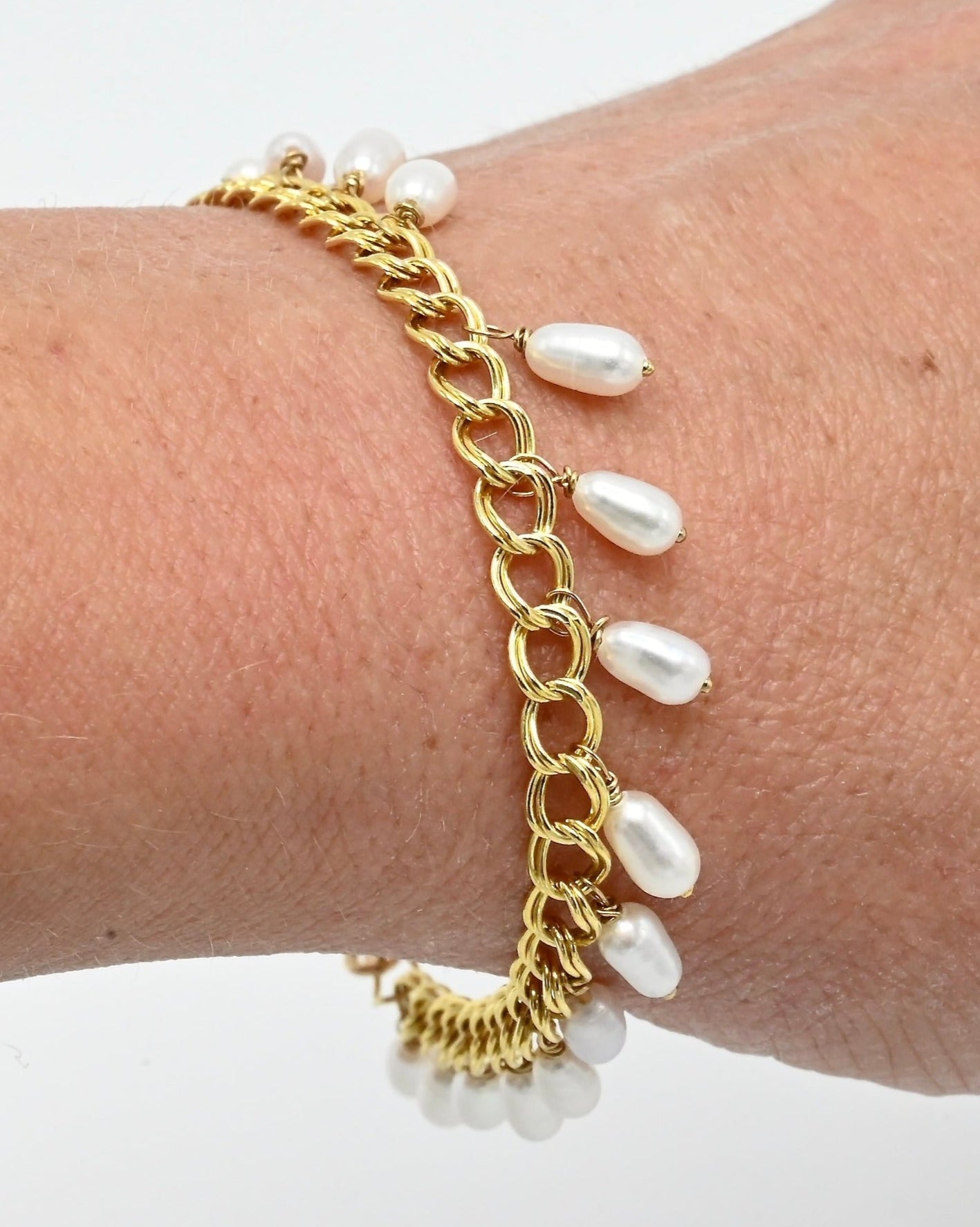 Gold chain bracelet with white pearls on a wrist against a white background